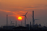 Sunset over industrial resort, with industrial park wind turbines, chimneys, factory buildings and high voltage pylons