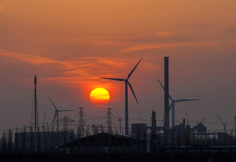 Sunset over industrial resort, with industrial park wind turbines, chimneys, factory buildings and high voltage pylons